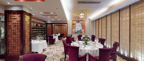 A dining area with round tables, red upholstered chairs, and a patterned carpet.