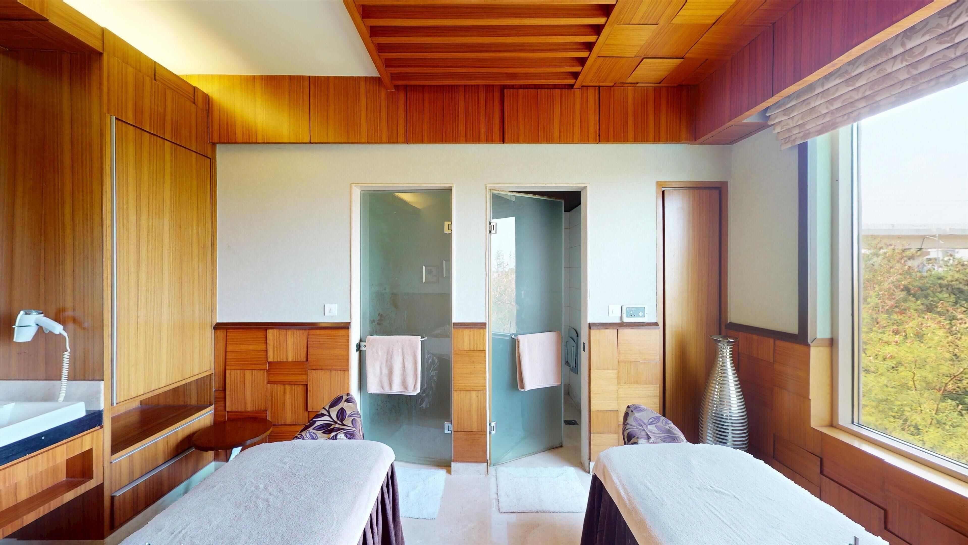 A room with wooden paneling, a large window, two beds with towels, a mirror, and a sink.