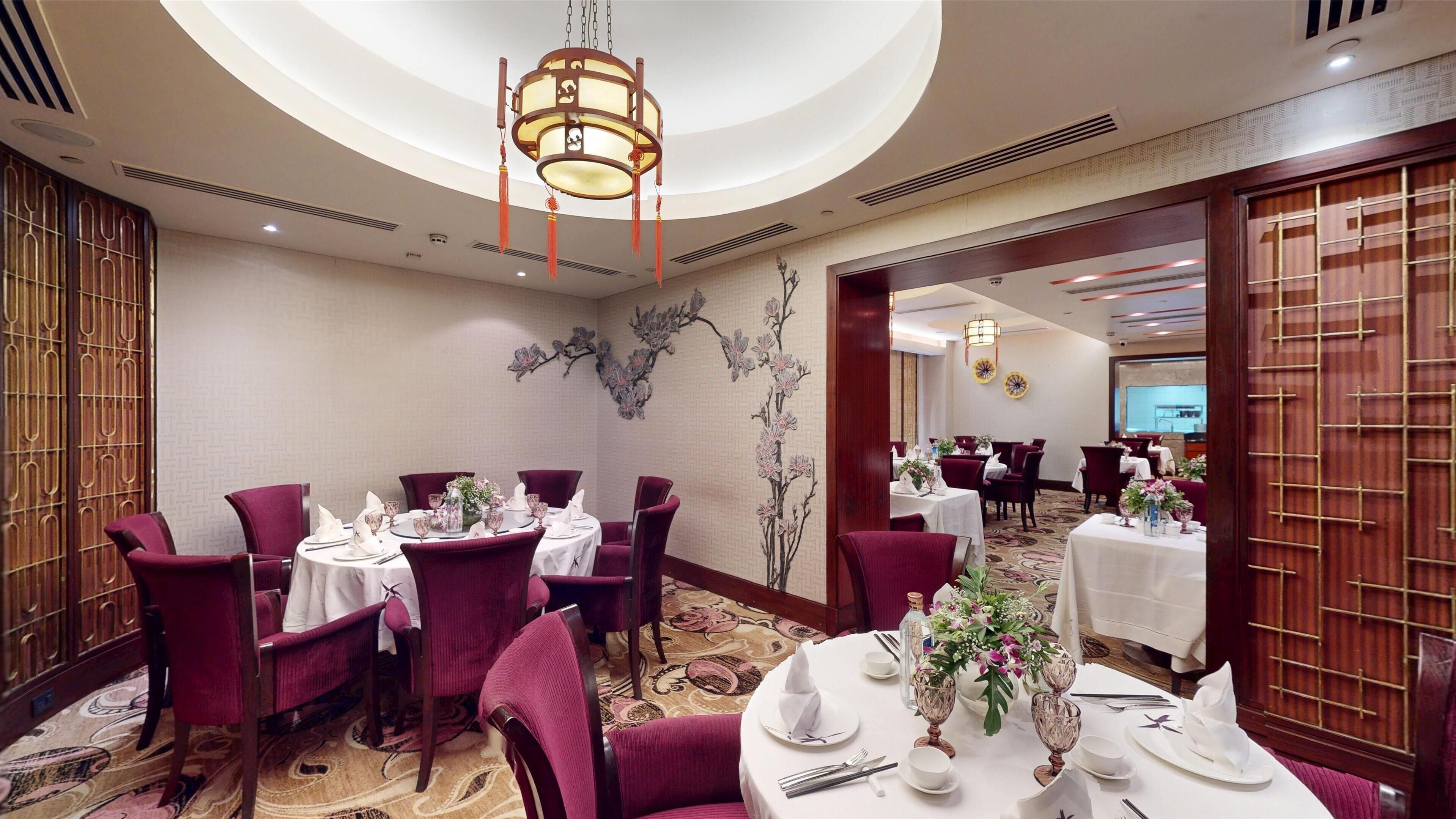 A dining area with round tables, red chairs, and a chandelier.