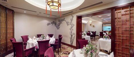 A dining area with round tables, red chairs, and a chandelier.