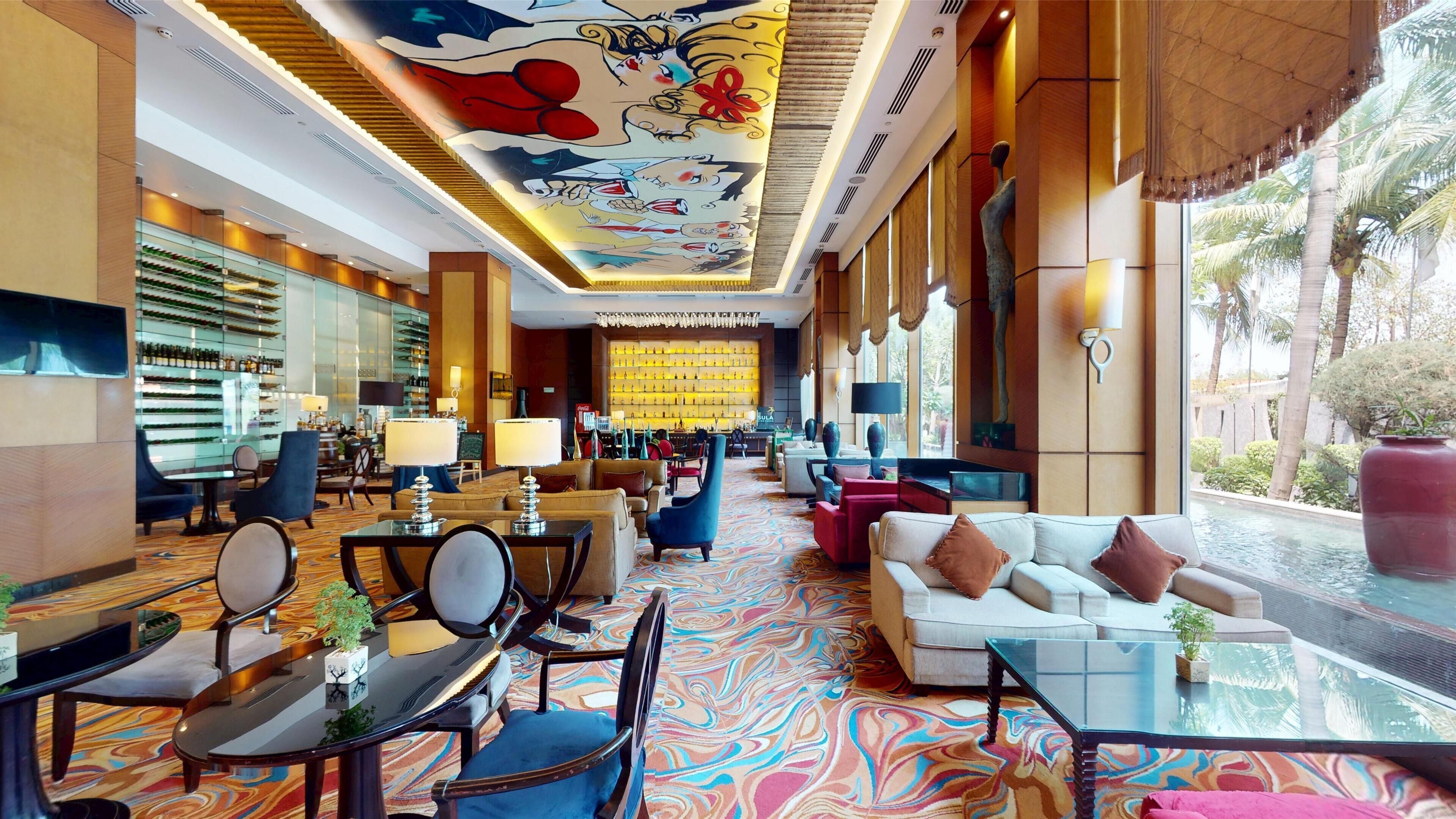 A hotel lobby with a bar area, seating arrangements, and a large mural on the ceiling.