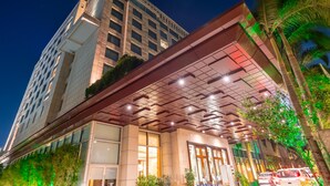 A modern hotel with a glass facade, a covered entrance, and a view of a tall building in the background. - Radisson Blu Hotel Nagpur (Nagpur)