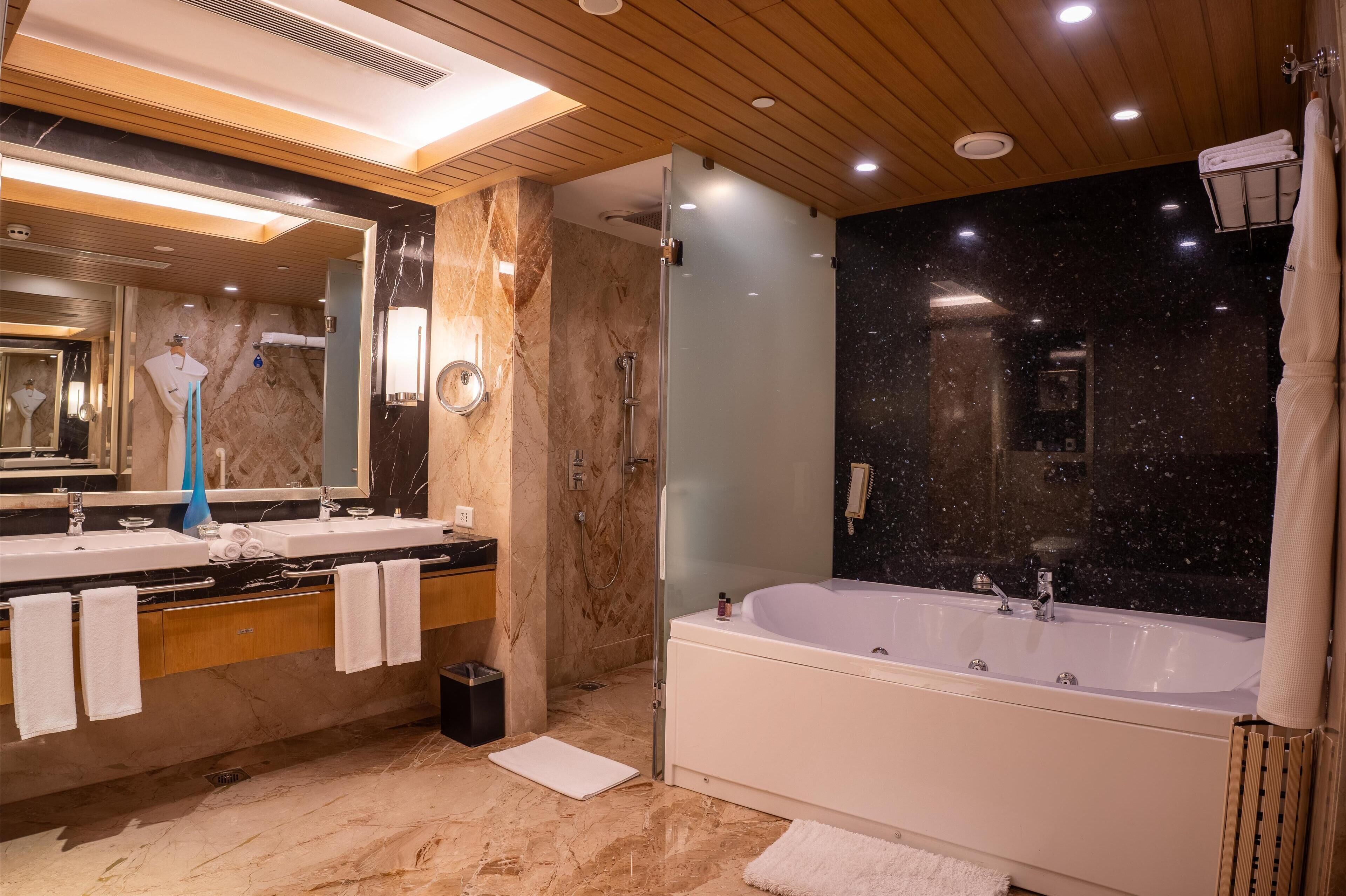 Un baño moderno con un espejo grande, dos lavamanos, una bañera y un box de ducha de vidrio.
