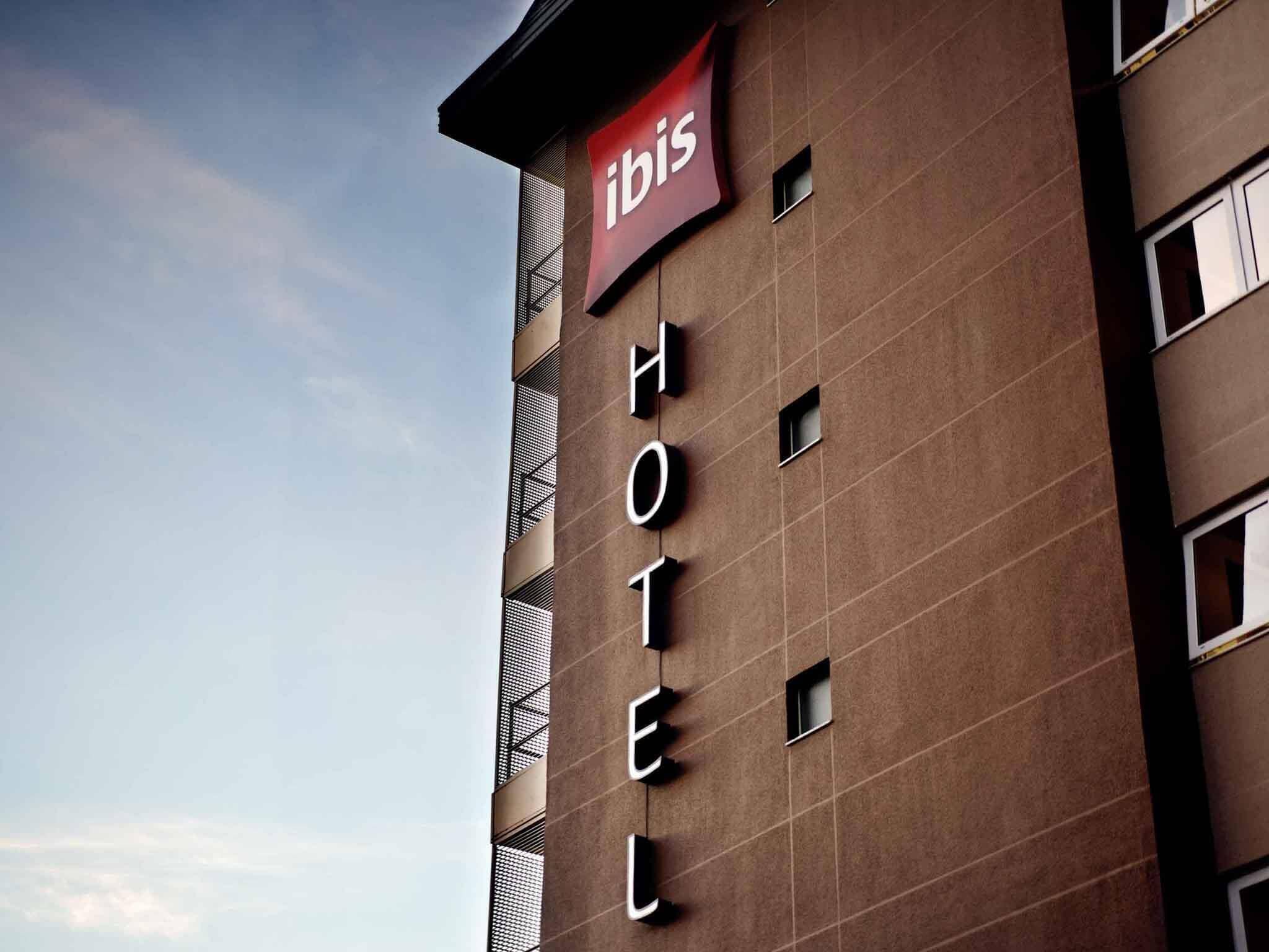 Un edificio de hotel con un letrero que dice 'ibis HOTEL' y un banderín rojo encima.