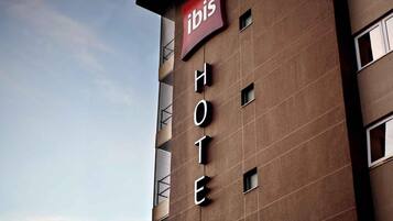 Un edificio de hotel con un letrero que dice 'ibis HOTEL' y un banderín rojo encima.