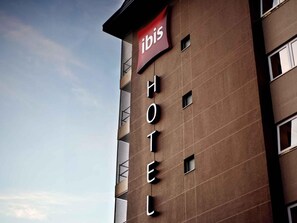 Un edificio de hotel con un letrero que dice 'ibis HOTEL' y un banderín rojo encima.