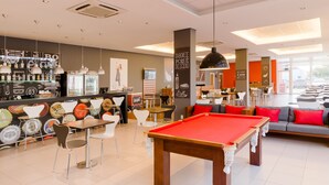 A billiards table, chairs, and a pool table in a modern lounge area with a bar and seating. - Ibis Canoas Shopping (Canoas)