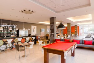 Una mesa de billar, sillas y una mesa de billar americano en un área de lounge moderna con bar y asientos.