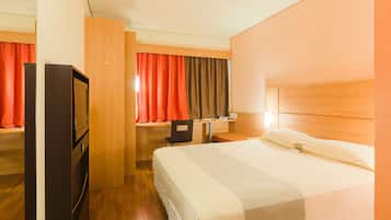 Una habitación de hotel con cama, escritorio, silla, televisor y armario.
