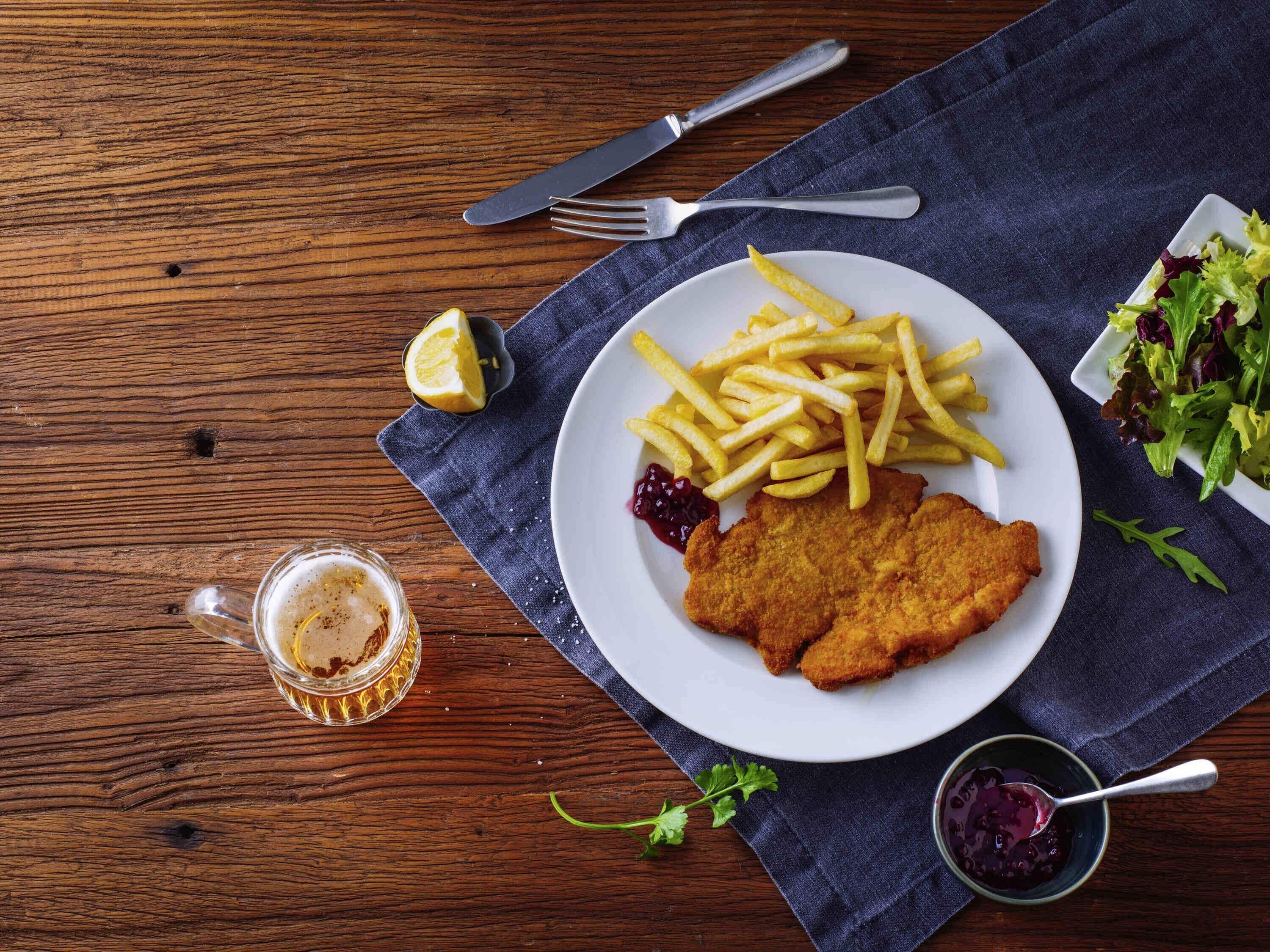A plate of food with fries, a breaded cutlet, and a side salad on a wooden table.
