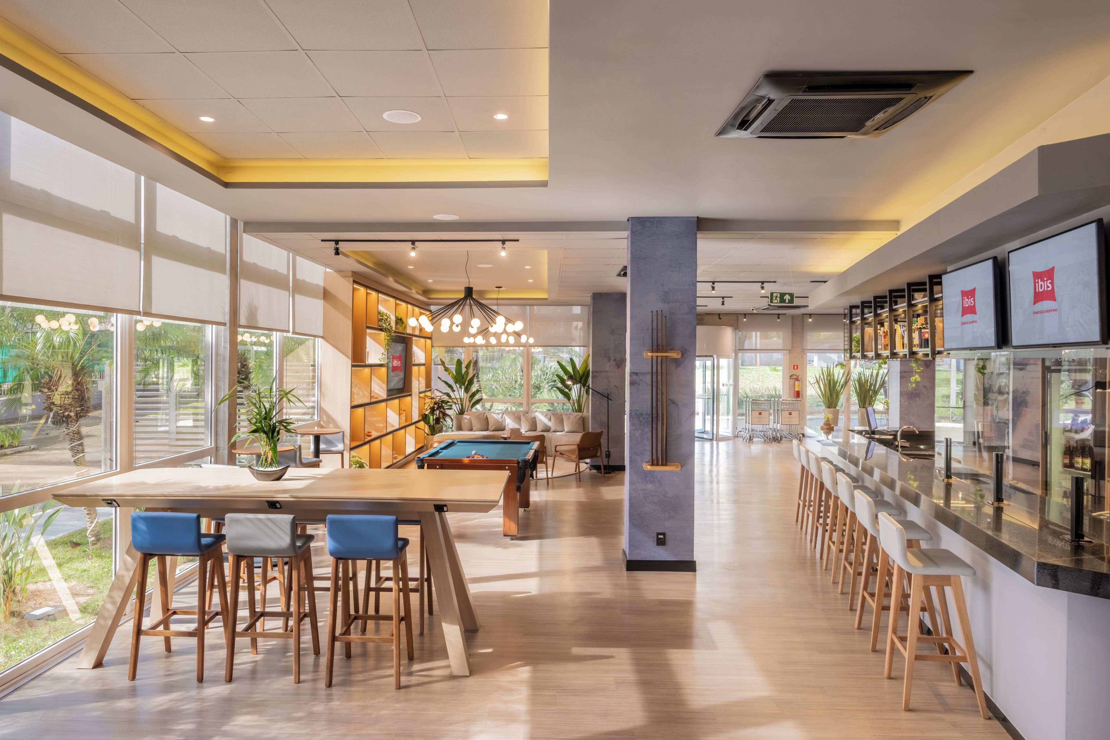 Un área de bar moderna con mesa de billar, taburetes y una zona de estar con sofá y sillones.