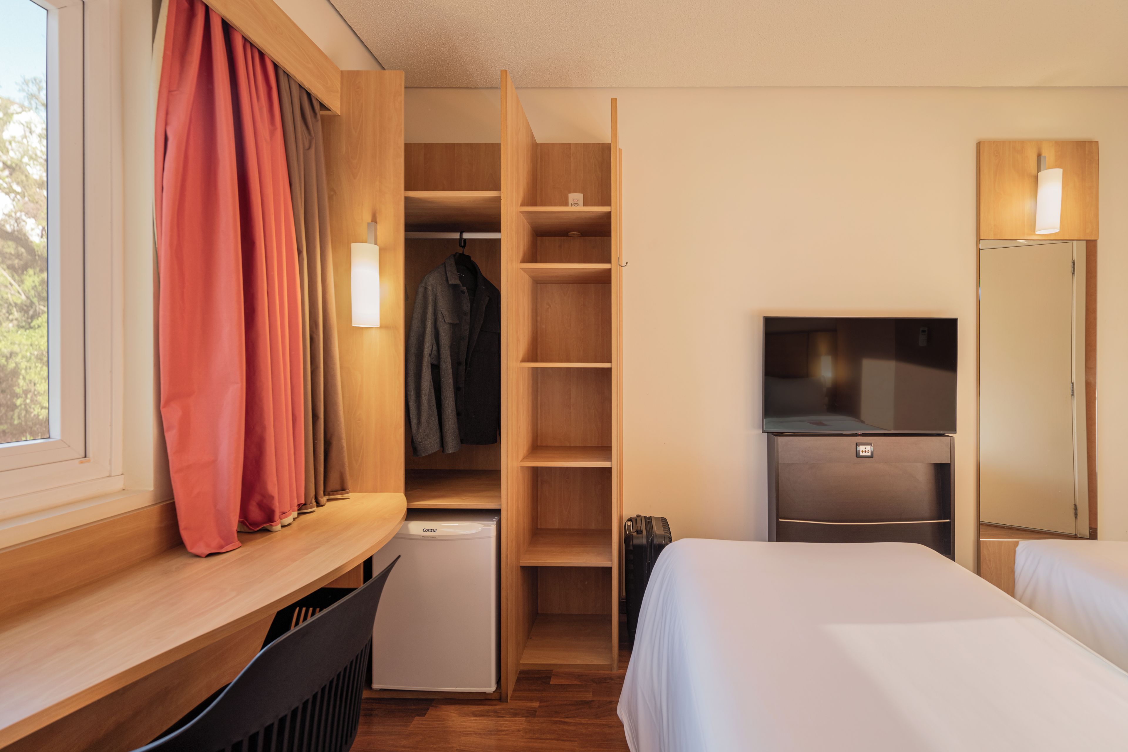 Una habitación de hotel con una cama, televisión, armario y un refrigerador pequeño.
