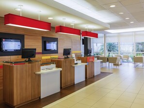 Uma área de recepção moderna com vários balcões de check-in, displays digitais e vista para o exterior.