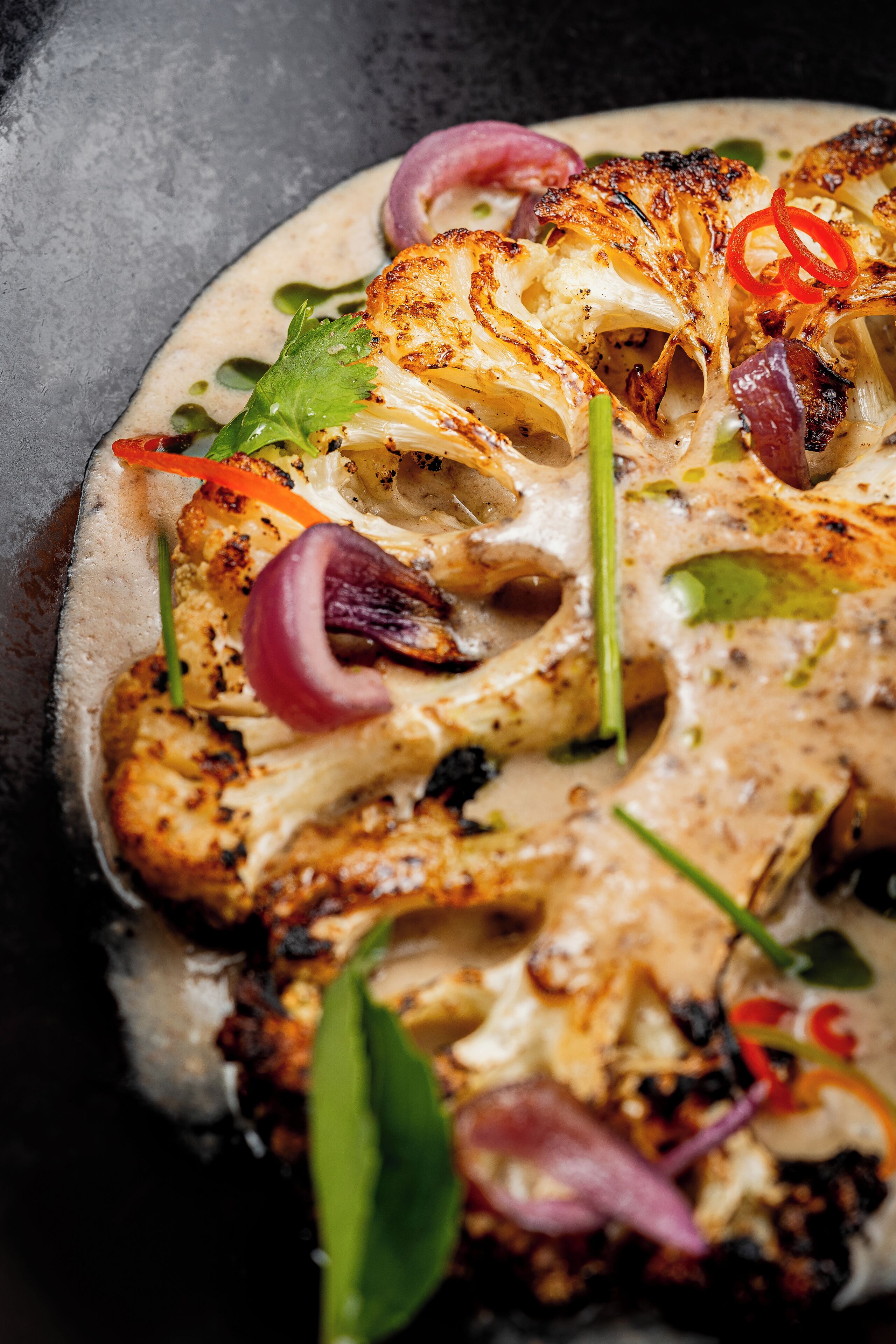 A close-up of a dish with grilled chicken, cauliflower, and red onions on a plate.