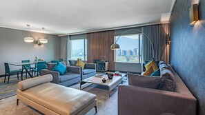 Une chambre d’hôtel moderne dotée d’un espace salon, d’un coin repas et de grandes fenêtres offrant une vue sur la ville.