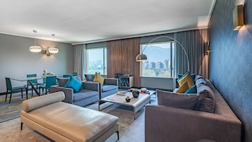 Una habitación de hotel moderna con zona de estar, comedor y grandes ventanales con vistas a la ciudad.