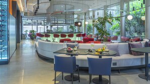 Een modern interieur met een gebogen zithoek, tafels met wijnglazen en een glazen wand met uitzicht op groen.