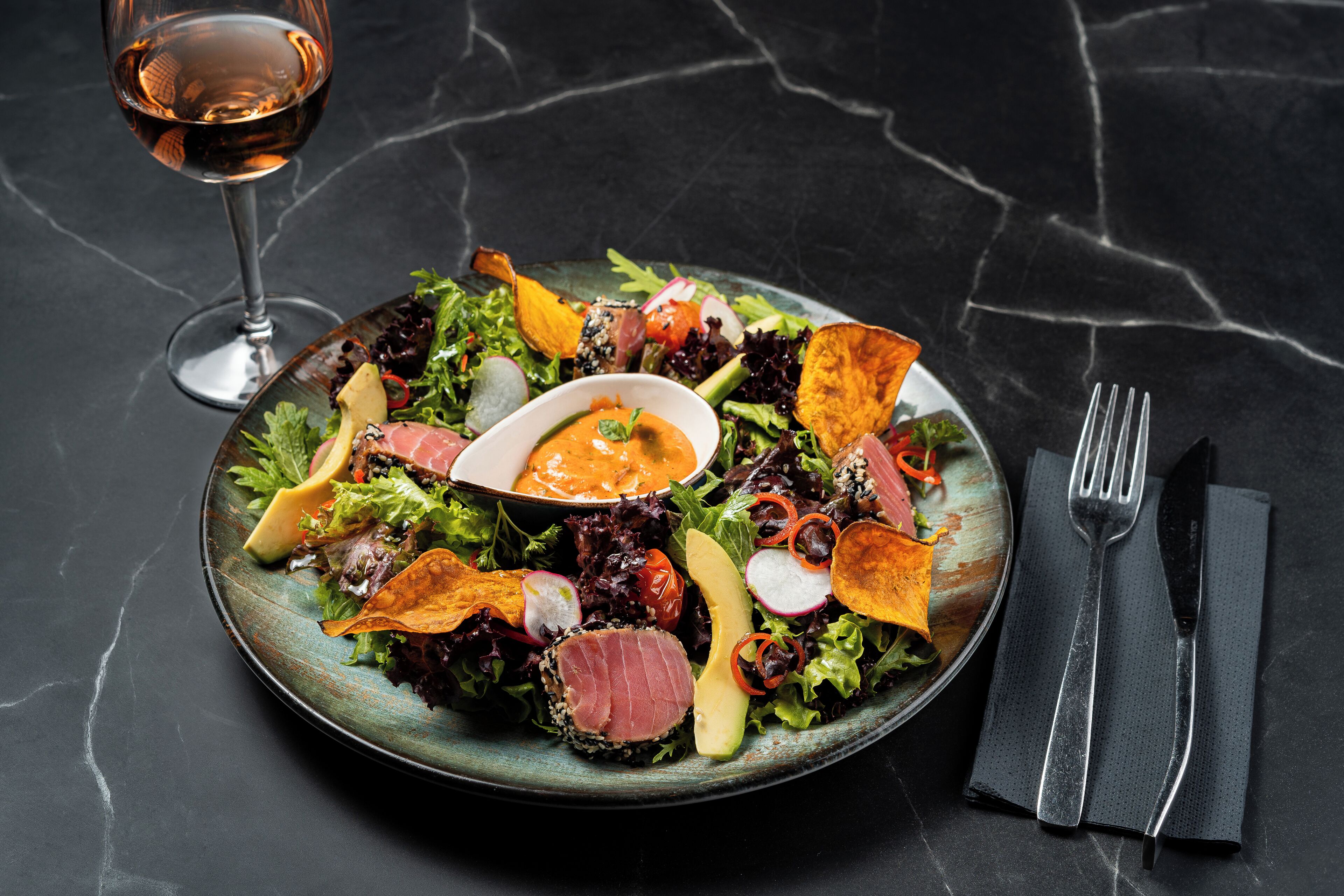 En salatskål med forskellige grøntsager og et glas vin på et mørkt marmorbord.