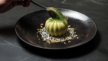 A hand using a spoon to serve a dish on a black plate.