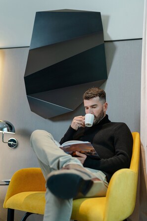 A man sitting in a yellow chair, reading a book, with a modern geometric wall design behind him. - Pullman Santiago Vitacura (Santiago)