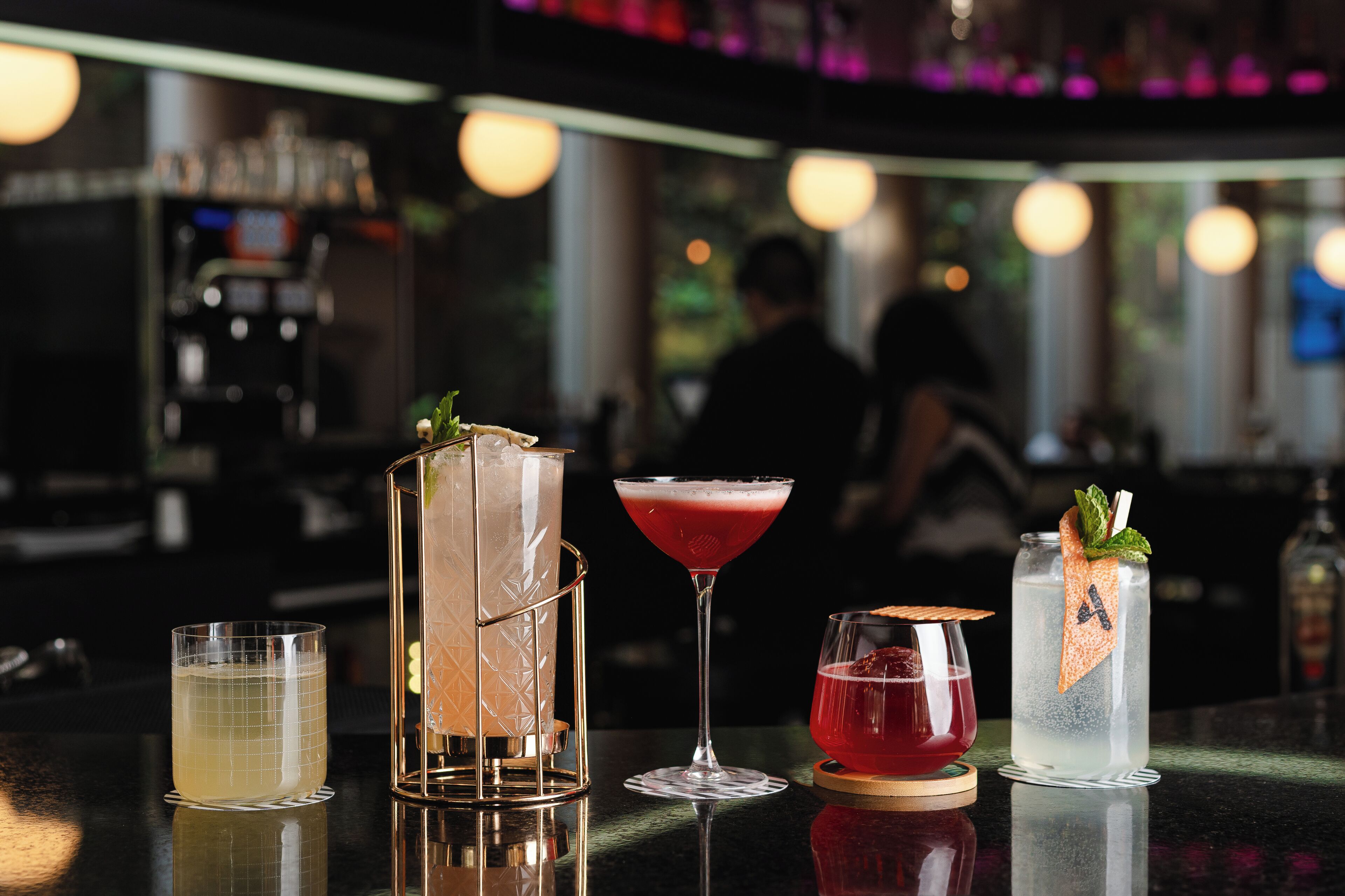 A bar with various drinks, including a martini, a cocktail with a red drink, and a clear drink with a mint garnish.