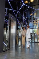 Un espacio interior con diseño moderno, que cuenta con un ascensor de vidrio y un patrón geométrico en el techo.