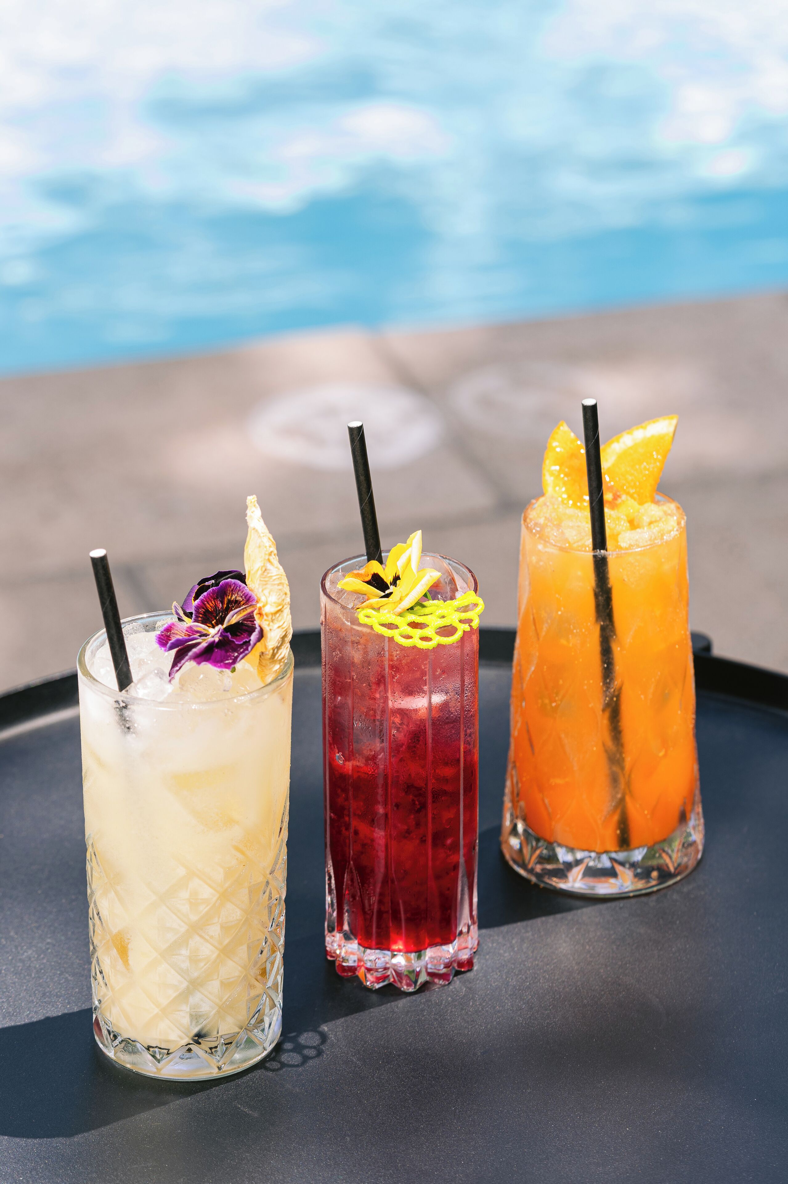 Tres bebidas sobre una bandeja junto a una piscina.