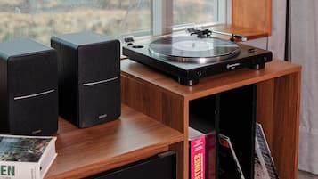 Un pupitre en bois pour partitions, équipé d’une platine et de haut-parleurs, ainsi que des livres et une fenêtre donnant sur des immeubles.