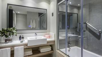 Un baño moderno con un espejo grande, un lavabo blanco, una ducha con mampara de vidrio y un tocador de madera.