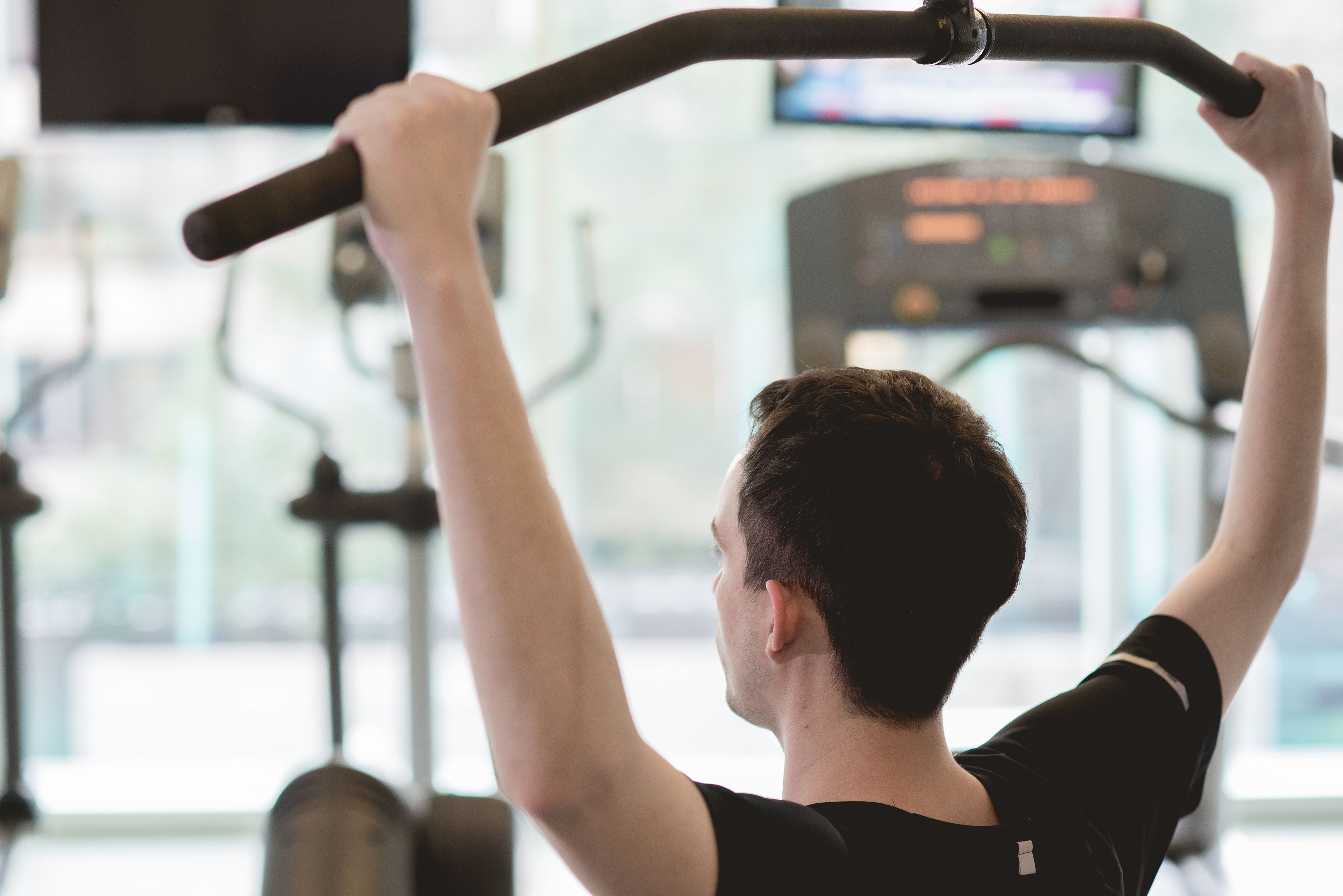 Una persona haciendo dominadas en un gimnasio, con una cinta de correr al fondo.