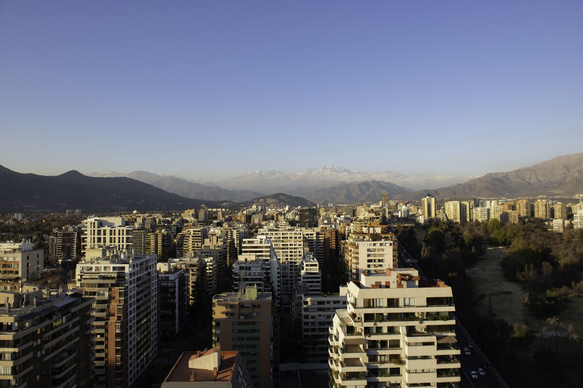 Un paisaje urbano con edificios altos, cielo despejado y montañas a lo lejos.