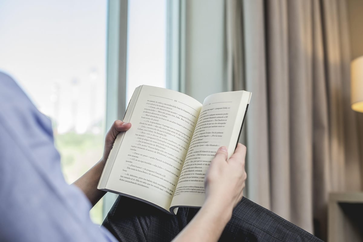 A person reading a book by a window with curtains.