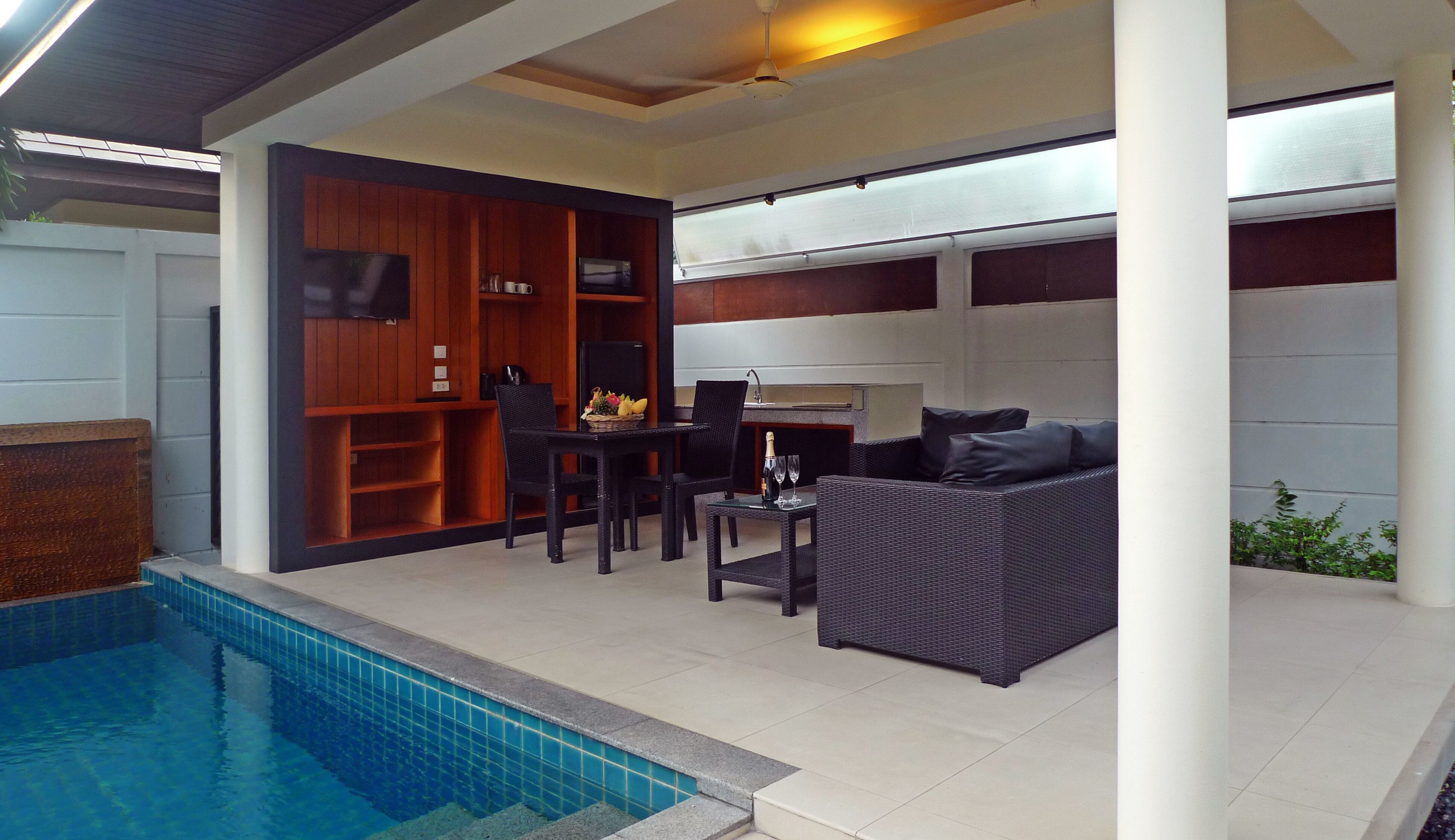 A modern outdoor living area with a pool, a dining table with chairs, a sofa, and a built-in kitchen area.