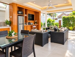 A modern outdoor kitchen area with a dining table, chairs, and a built-in wooden cabinet with appliances. - Samui Boat Lagoon (Koh Samui)