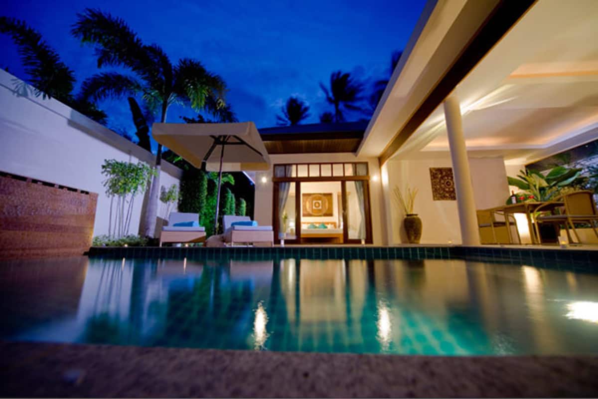 A modern pool area with a clear view of the pool, lounge chairs, and a well-lit interior space.