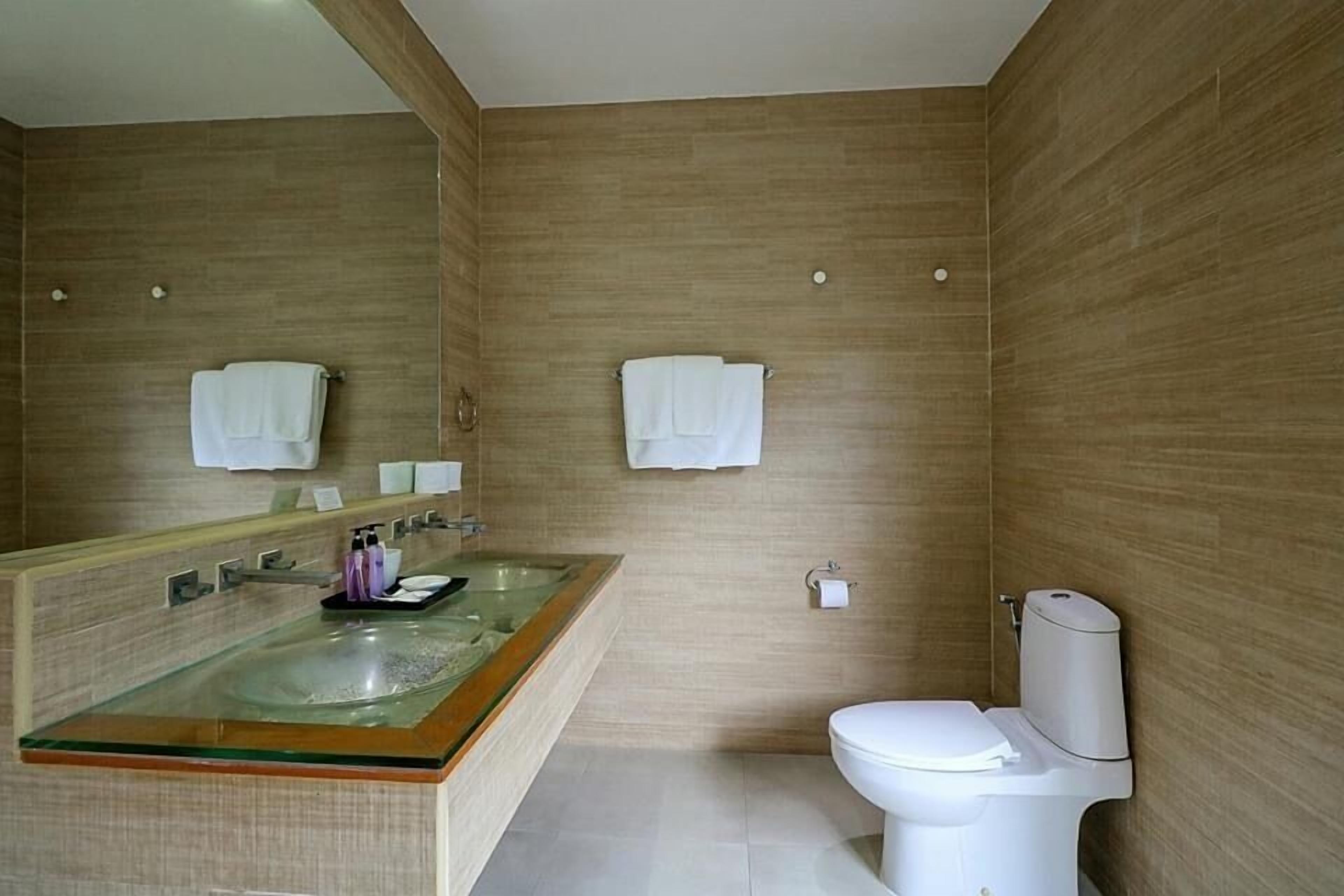 Un baño moderno con un lavabo de vidrio, un inodoro y paredes de madera.