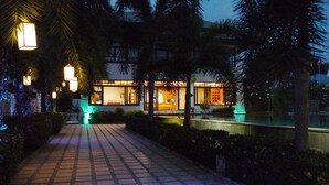 A modern building with large windows and a well-lit interior, surrounded by palm trees and a paved pathway. - Samui Boat Lagoon (Koh Samui)
