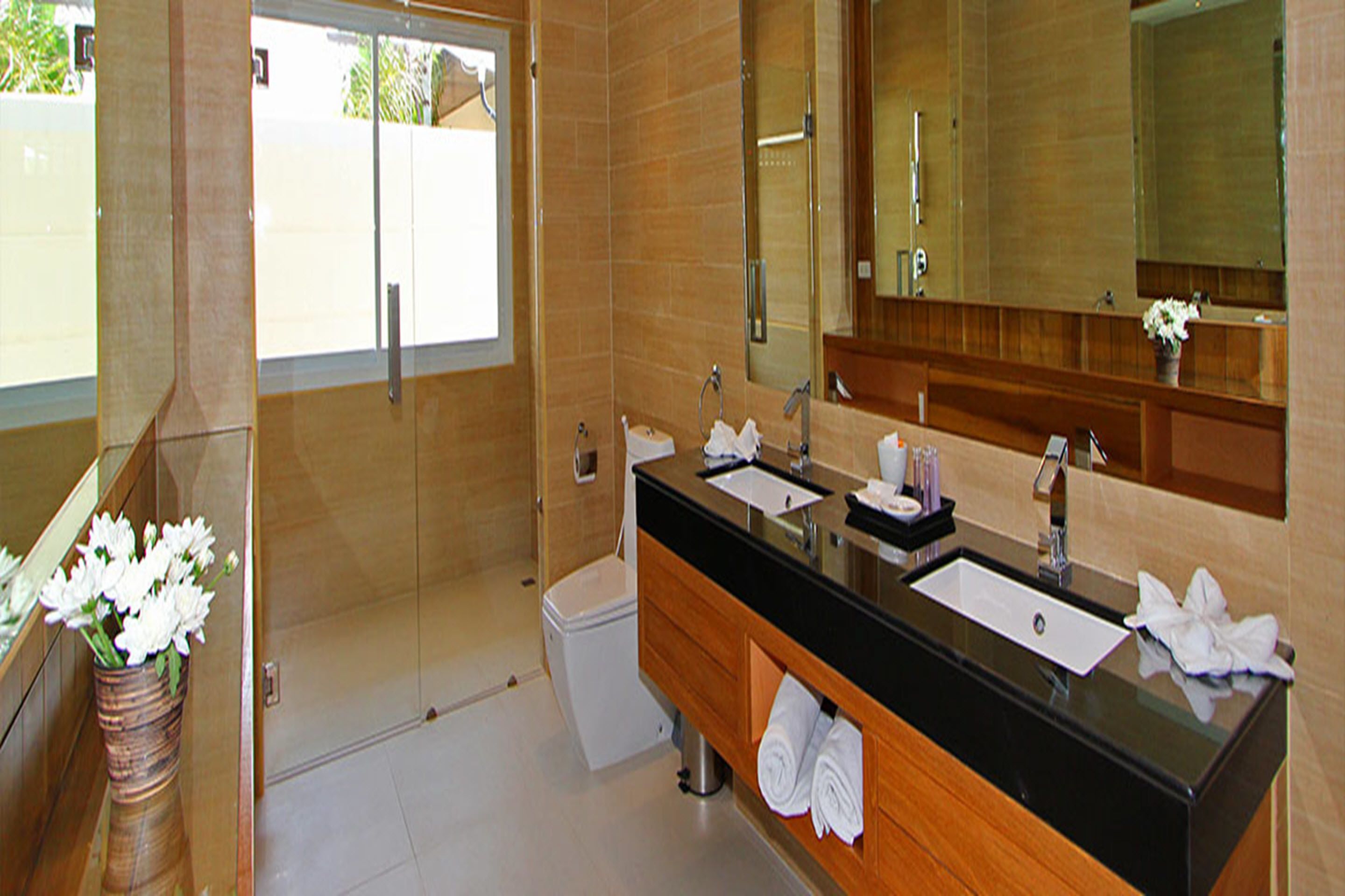 Une salle de bain moderne avec un plan de toilette noir, deux vasques, une douche et un meuble-lavabo en bois.