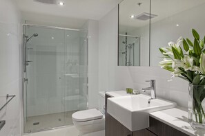 A modern bathroom with a glass shower enclosure, a white toilet, a vanity with a sink, and a mirror. - Mantra Midtown (Brisbane)