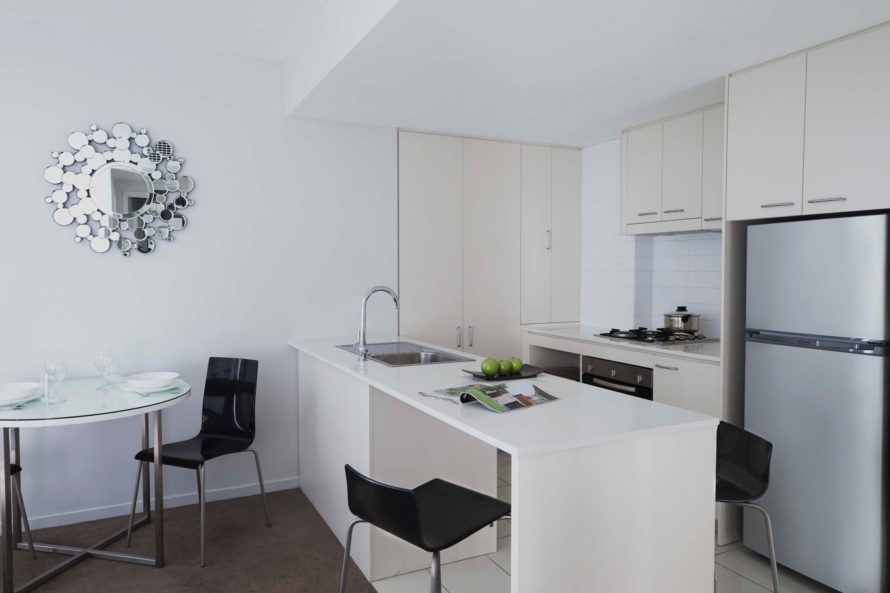 Una cucina moderna con mobili bianchi, un frigorifero in acciaio inossidabile e un tavolo da pranzo in vetro con due sedie.