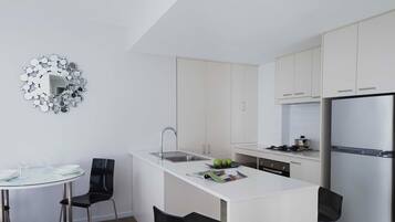 Una cucina moderna con mobili bianchi, un frigorifero in acciaio inossidabile e un tavolo da pranzo in vetro con due sedie.
