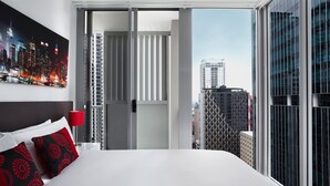 A hotel room with a bed, a red lamp, a cityscape view, and a large window. - Mantra Midtown (Brisbane)