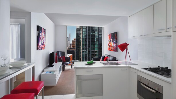 A modern kitchen with white cabinets, a gas stove, and a dining area with red chairs. - Mantra Midtown (Brisbane)