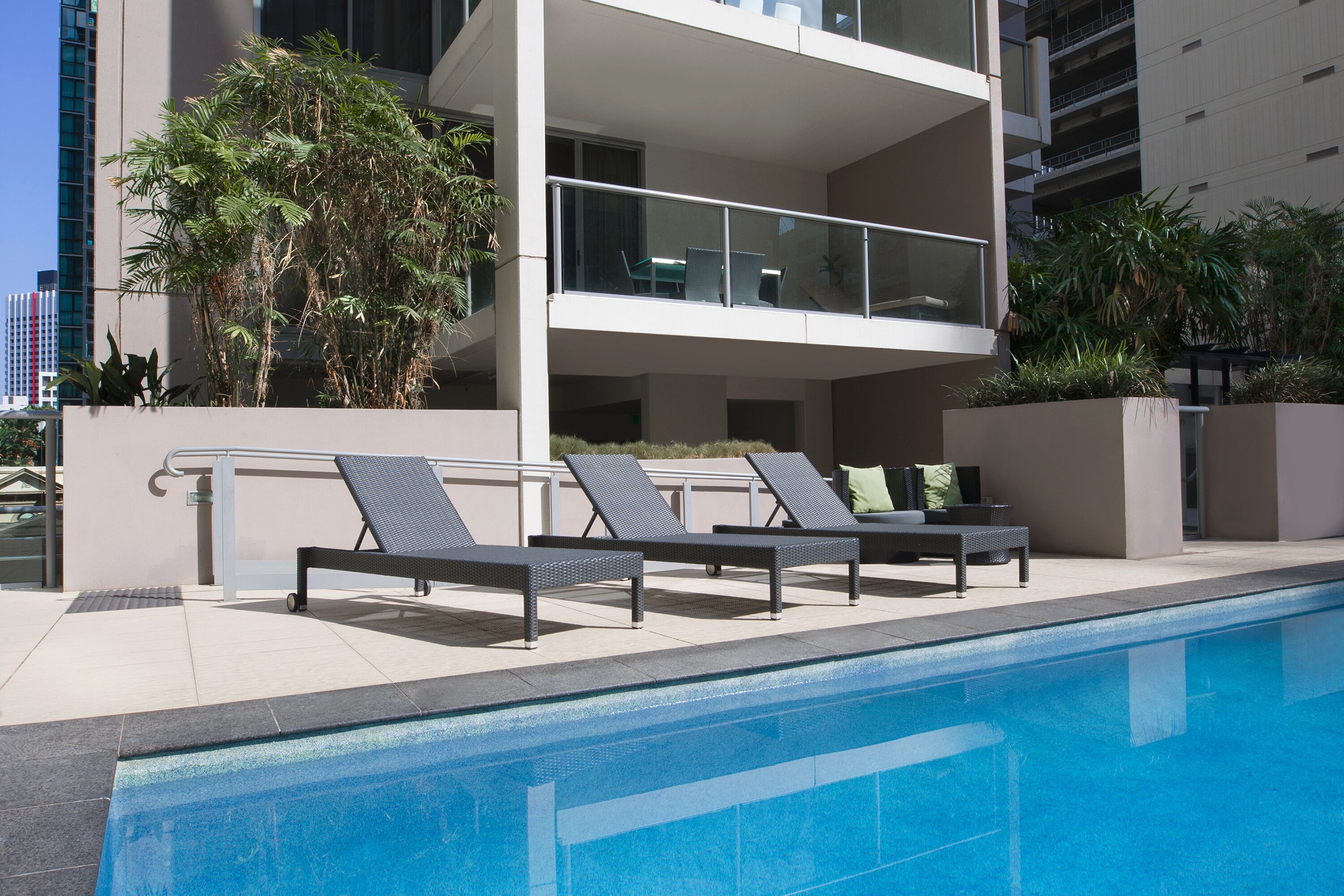 A modern building with a rooftop pool area, featuring lounge chairs and potted plants.