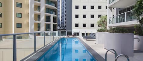Ein moderner, überdachter Swimmingpool mit Glasrelings, umgeben von mehrstöckigen Wohngebäuden mit Balkonen.