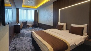 A hotel room with a large bed, a desk, a chair, and a television.
