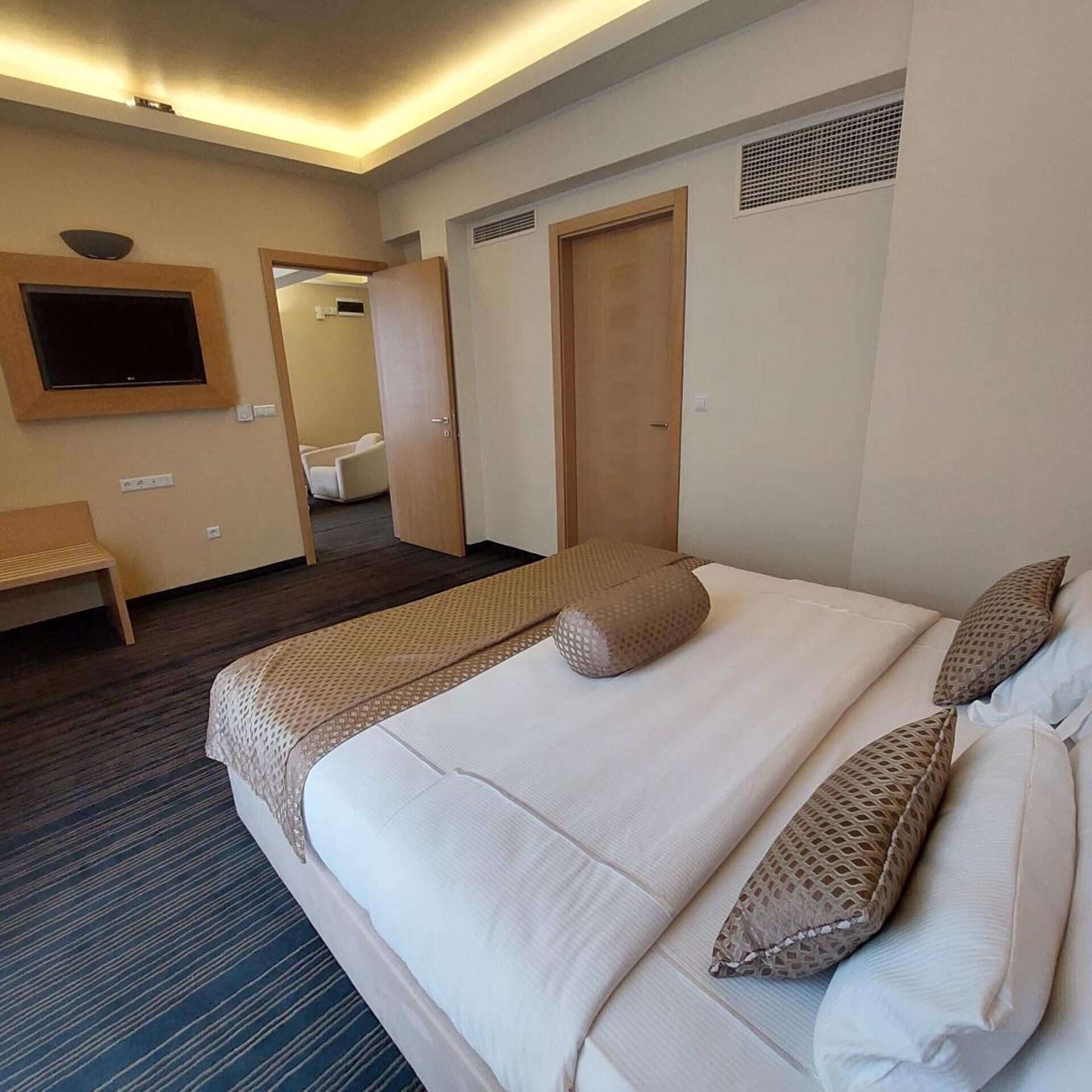 A hotel room with a large bed, a TV mounted on the wall, and a door leading to a bathroom.