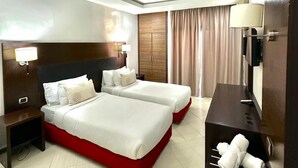 Une chambre d’hôtel avec deux lits, un bureau, une chaise, une télévision et une salle de bain équipée d’un porte-serviettes.