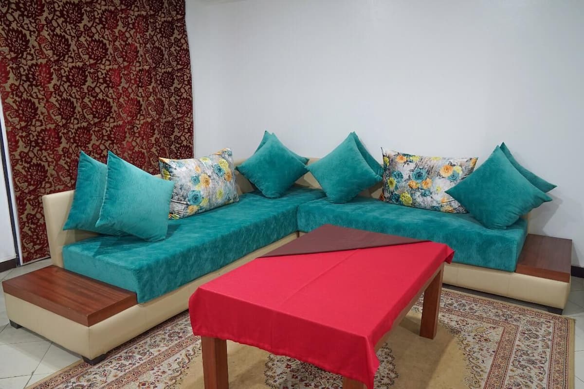Ein Wohnzimmer mit einer Sofagarnitur, einem roten Tisch und Teppichen mit Muster.