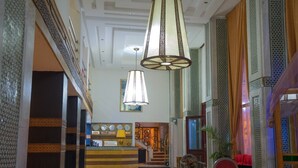 Un hall d’entrée spacieux avec un comptoir d’accueil, un escalier et un grand lustre.